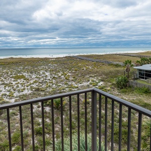 Balcony view showcases lush greenery leading to the beach, with gentle waves and a tranquil atmosphere in the distance