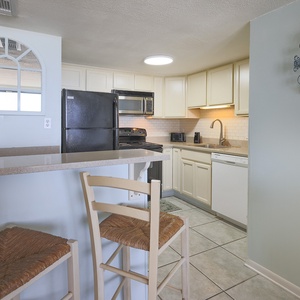 The kitchen features light cabinetry, essential appliances, and a breakfast bar perfect for casual dining