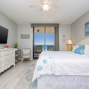 Master suite featuring a king bed, a flat-screen TV, and access to a balcony with a view of the beach