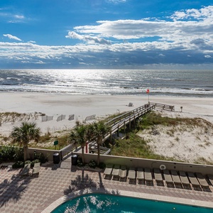 This inviting view showcases the beachfront, poolside lounging area, and lush palm trees, perfect for relaxation