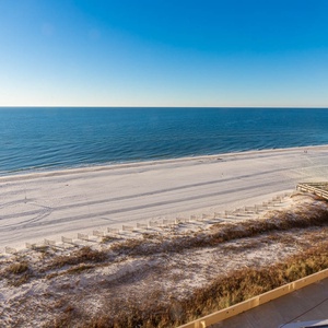 Expansive view of the tranquil beach with white sand and gentle waves, framed by a clear blue sky and serene atmosphere