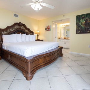 Elegant master bedroom featuring a king-size bed with decorative headboard, nightstand lamp, and an en-suite bathroom