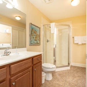 The extra bath features a stylish walk-in shower, a spacious vanity, coastal artwork, and laundry area with washer and dryer