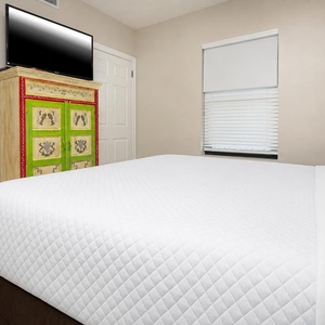 Rest in this guest room featuring a comfortable king bed, a colorful dresser, and a mounted TV for your entertainment