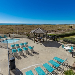 Inviting pool area features turquoise lounge chairs, a kiddie pool, and a gazebo, with a scenic view of the beach beyond