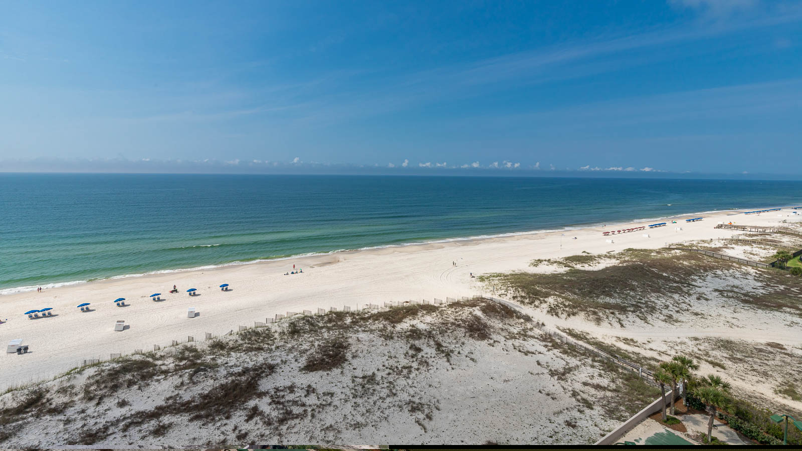 Gaze at the inviting shoreline, where colorful umbrellas dot the beach and gentle waves create a serene atmosphere
