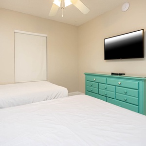 Cozy guest room featuring two comfortable double beds, a vibrant dresser, and a mounted TV for your entertainment