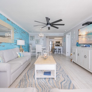 Living area featuring a light gray sofa with queen sleeper and decorative accents that lead to the dining and kitchen area