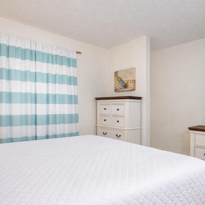 Relax in the plush queen bed, enjoying serene moments with coastal artwork and cozy vibes in the master suite