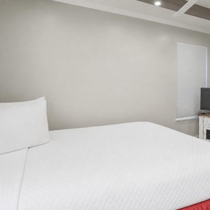 This guest bedroom features a cozy red bed, a TV for entertainment, and a bright atmosphere with natural light