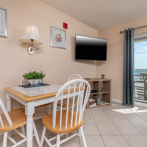 This cozy dining area features a TV, a table for meals, and a stunning view of the beachfront through sliding glass doors