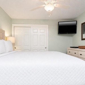 This guest bedroom features a cozy white queen bed, a wall-mounted TV, and stylish cabinetry for a relaxing retreat