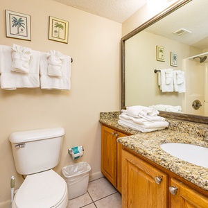 The guest bathroom features a tub/shower combo, granite countertop, and neatly stacked towels for a refreshing experience