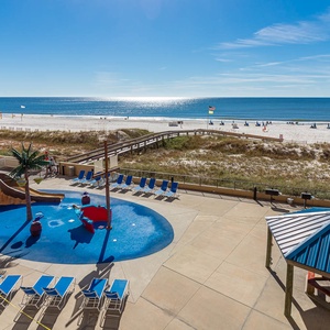 The pool area features a vibrant splash park by the pool and lounge chairs, with a serene view of the beach and calm waters