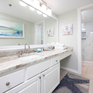 The master bath features a marbled countertop with a stylish sink, fresh towels, and a walk-in shower with elegant tile work