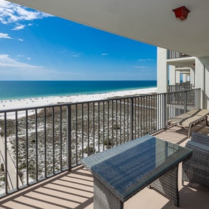 Balcony with a glass table and seating offers a serene view of the beach and vibrant gulf waters under a clear blue sky