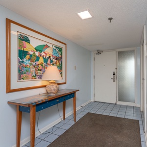 Colorful artwork adorns the wall above a wooden console table with a lamp, welcoming guests into the bright entryway