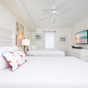 Bright guest bedroom featuring two queen beds, a TV, and colorful artwork, creating a cheerful and relaxing atmosphere
