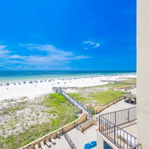 Vibrant beach view with white sand and blue umbrellas, framed by a clear blue sky and lush greenery