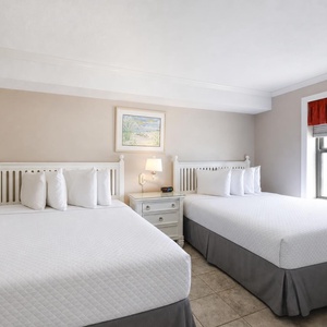Two queen beds in the guest room with decorative pillows are complemented by a bedside table and a window