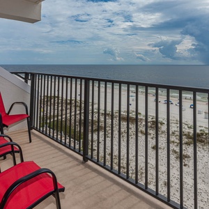 Enjoy a relaxing view from the balcony with red chairs overlooking the beach and gentle waves in the distance