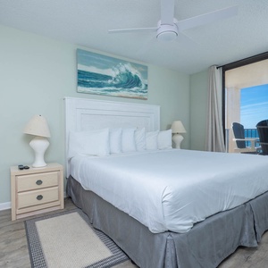 Brightly decorated master bedroom features a king bed, coastal artwork, and sliding glass doors leading to a balcony