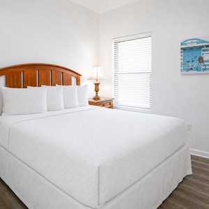 Bright and inviting guest bedroom featuring a cozy wooden queen bed, soft white linens, and a charming beach-themed artwork