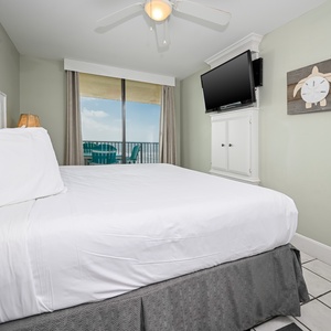 A cozy master bedroom features a plush king bed, flat-screen TV, and a balcony view with seating overlooking the beach
