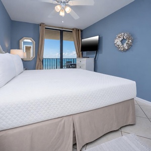 Master bedroom featuring a king bed, modern TV, and breathtaking beach views from the balcony