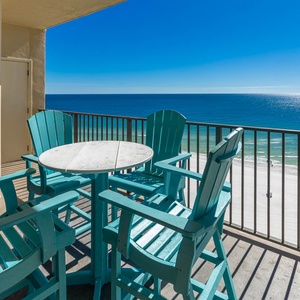 Balcony features turquoise Adirondack chairs surrounding a round table, overlooking the tranquil beach and sparkling waters