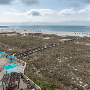 View of the pool area with turquoise loungers, leading to the beach, framed by lush greenery and a wooden walkway