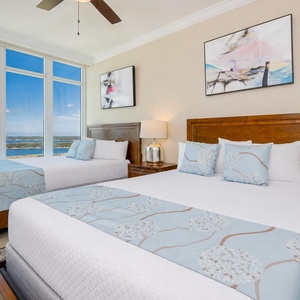 Guest suite invites you to rest on two queen beds while watching boats drift on shimmering blue waters beyond tall windows