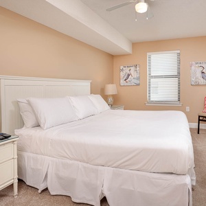 Guest bedroom featuring a king bed, light beige walls, decorative beach artwork, and a mounted TV