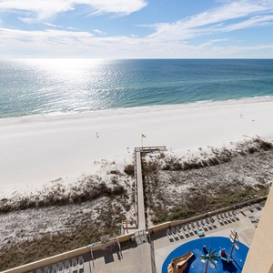 The view showcases a serene beach with white sand, framed by gentle waves and a clear blue sky, inviting relaxation