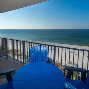 Relax in vibrant blue chairs on the balcony, enjoying expansive views of the tranquil water and beach below