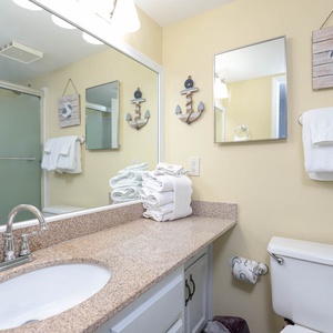The guest bath features a stylish granite countertop, a glass shower, and nautical decor for a refreshing retreat