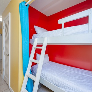 This colorful sleeping nook features a white bunk bed against a vibrant red wall, creating a fun space for kids or guests