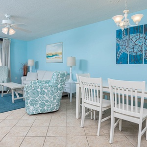 Brightly colored living area features a comfortable sofa, patterned chair, dining table, and expansive views of the gulf