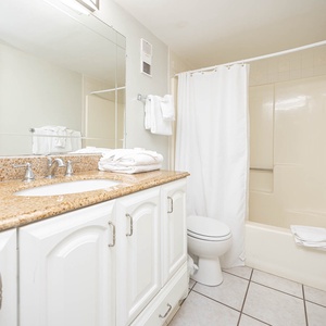 This bathroom features a sleek granite countertop, bright white towels, and a clean, inviting shower space