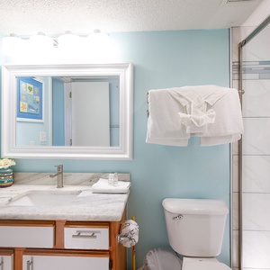 Bright bathroom featuring a marbled countertop, a walk-in shower, and cheerful coastal artwork on the walls