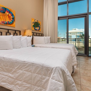 This bright guest bedroom features two full beds, vibrant coastal artwork, and large windows for a refreshing view