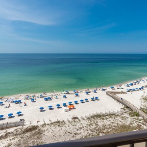 A panoramic view reveals vibrant blue umbrellas lining a pristine beach with soft white sand under a clear blue sky