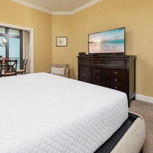 Master bedroom featuring a king bed, a large TV, and a view of the dining area with elegant chandelier lighting
