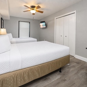 Bright guest room featuring two queen beds, a ceiling fan, wall-mounted TV, modern decor and natural light