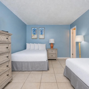 Inviting guest bedroom featuring a double and a twin bed, TV, and colorful beach artwork on soft blue walls