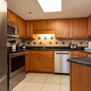 The kitchen features warm wood cabinetry, black countertops, and stainless appliances for a seamless cooking experience