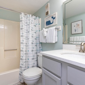 The bathroom features a light blue accent wall, a modern vanity with a spacious countertop, and a charming whale-themed decor