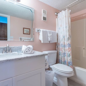 The bathroom features a light color scheme, a spacious granite countertop, relaxing tub, and a shower curtain with seashells