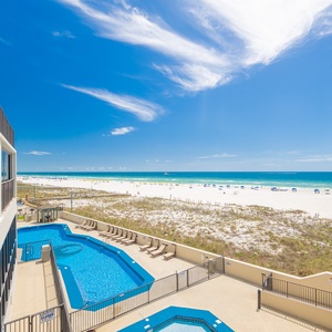 Turquoise pool water sparkles below while you watch colorful umbrellas dot the beach