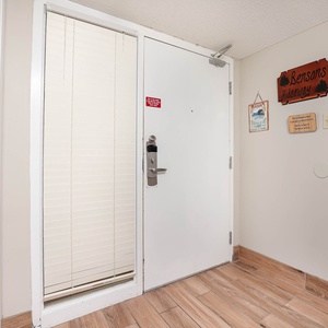 The entryway features a white door with a secure lock, light wood flooring, and decorative signs on the wall